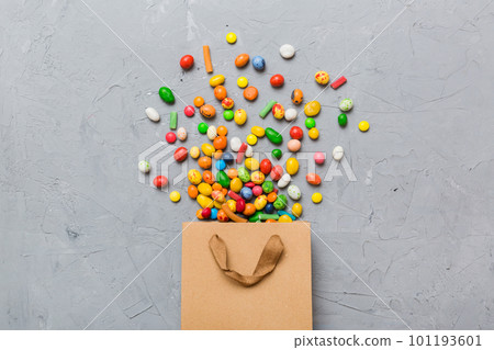 shopping paper gift bag in corner full of assorted traditional candies falling out on colored background with copy space. Happy Holidays sale concept 101193601