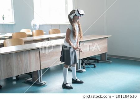 Caucasian schoolgirl wearing virtual reality glasses in the classroom.  101194630