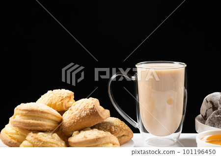 Tea with milk in a glass cup with a double bottom and cakes on a black background, place for text Tea with milk in a glass cup with a double bottom and cakes on a black background, place for text 101196450