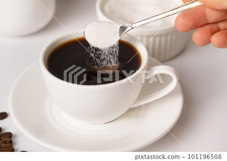 The process of pouring white sugar from a spoon into a white cup of coffee. Sugar addict, diabetes. The process of pouring white sugar from a spoon into a white cup of coffee. Sugar addict, diabetes. 101196508