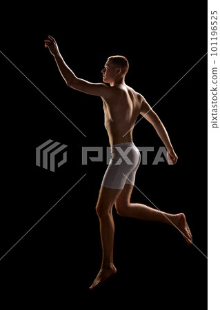 Portrait of young attractive redhead man wearing underwear and jumping in unusual posture over dark background 101196525