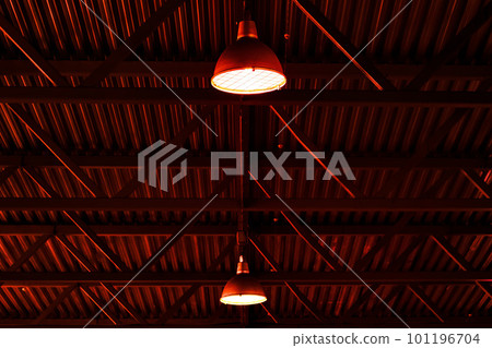 Gloomy red lighting in industrial hangar. Industrial luminaires or lampshades hang under roof inside 101196704
