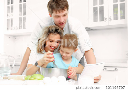 Young Caucasian family of three cooks lunch or festive cake in kitchen according to recipe. Happy Young Caucasian family of three cooks lunch or festive cake in kitchen according to recipe. Happy 101196707