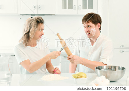 Husband and wife quarrel in kitchen while cooking. Comic and cheerful confrontation between man and Husband and wife quarrel in kitchen while cooking. Comic and cheerful confrontation between man and 101196708