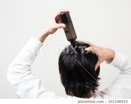 Back view of a man who applies a hair restorer to his hair / scalp care 101196933