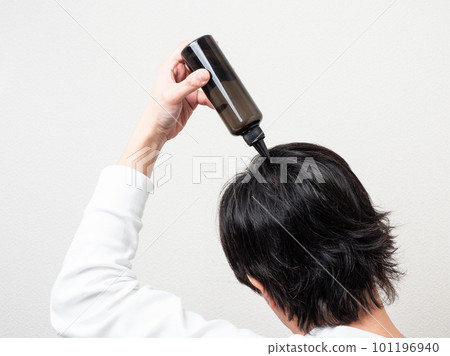 Back view of a man who applies a hair restorer to his hair / scalp care 101196940