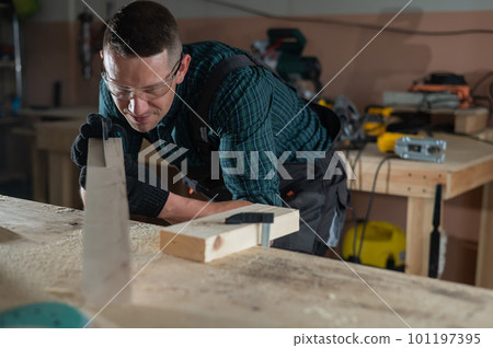 Carpenter measures a wooden board while working in a workshop.  101197395