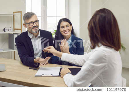Happy couple receives keys to their own house from female worker in real estate agency. Happy couple receives keys to their own house from female worker in real estate agency. 101197978