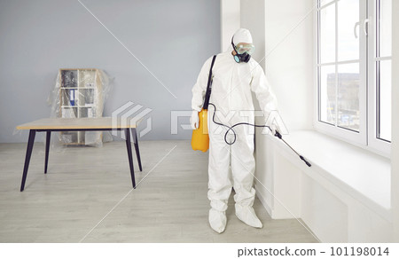 Man wearing protective ppe suit, glasses and face mask disinfecting office with disinfectant spray. 101198014