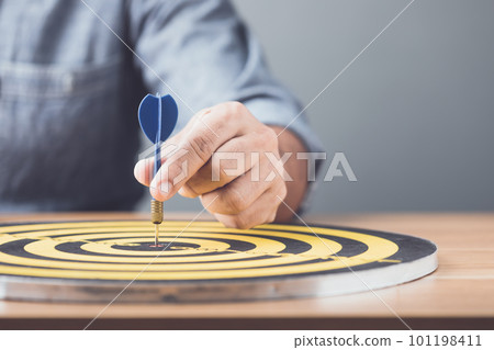 Businessman working in the office and throwing arrow darts in the center of yellow dartboard. Goal and success for business concept. 101198411