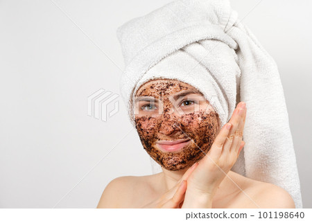A beautiful young woman with a bath towel on her head and a coffee mask on her face takes care of her skin 101198640