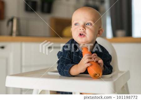Little boy in a blue t-shirt sitting in a child's chair eating carrot copy space and empty space for text - baby care and infant child feeding concept Little boy in a blue t-shirt sitting in a child's chair eating carrot copy space and empty space for text - baby care and infant child feeding concept 101198772