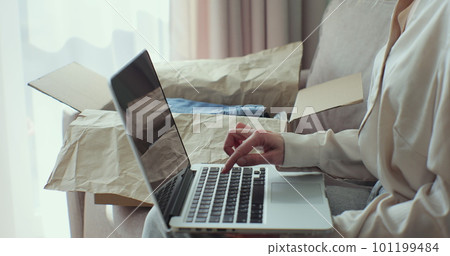 Woman customer shopper receiving online shop purchase and checks order on laptop. Happy female unpacking parcel box at home. Woman customer shopper receiving online shop purchase and checks order on laptop. Happy female unpacking parcel box at home. 101199484