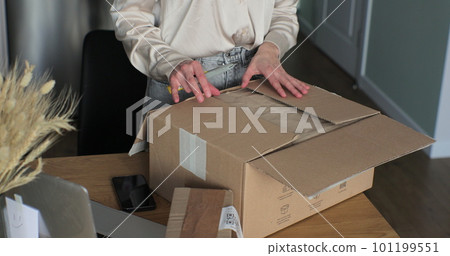 Woman consumer cutting order box on table at home room. Closeup view of female cuts cardboard and uses knife in hand. Happy client of online retailer concept. Woman consumer cutting order box on table at home room. Closeup view of female cuts cardboard and uses knife in hand. Happy client of online retailer concept. 101199551