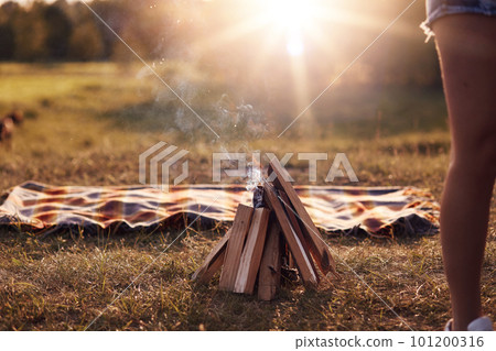 Campfire on green grass, plaid lies near, beautiful nature, calm atmosphere, sunshine, no people on photo. Summer vacation, picnic, lifestyle, leisure and lifestyle concept 101200316