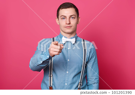 Handsome serious confident young man stands isolated over pink background in studio, rising his arm, showing direction with his forefinger, looks decisive and strong. People and emotions concept. Handsome serious confident young man stands isolated over pink background in studio, rising his arm, showing direction with his forefinger, looks decisive and strong. People and emotions concept. 101201390