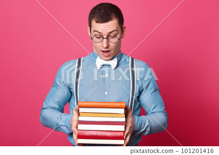 Close up portrait of interested surprised young man looking with shock at cover of top book, reading headline attentively, opening his mouth and eyes widely, holding bunch of various books in hands. Close up portrait of interested surprised young man looking with shock at cover of top book, reading headline attentively, opening his mouth and eyes widely, holding bunch of various books in hands. 101201416
