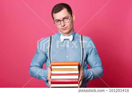 Tired athletic upset young man looks directly at camera, posing isolated over pink background, looks disappointed, wearing blue shirt, white bowtie, striped suspenders and fashionable spectacles. 101201418