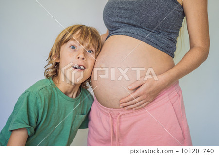 Young beautiful pregnant woman and eldest son. The cute boy leaned his ear against his mother's belly. Expecting a baby in the family concept. Preparing an older child for a younger one 101201740