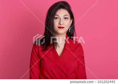 Fashion model wearing red dress, elegance woman standing and looking directly at camera, studio shot of brunette female posing isolated over pink background, lady with dark hair and bright red lips. Fashion model wearing red dress, elegance woman standing and looking directly at camera, studio shot of brunette female posing isolated over pink background, lady with dark hair and bright red lips. 101202445