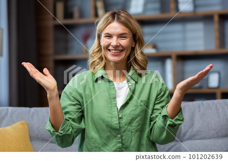Portrait of a scared happy curvy woman sitting at home on the sofa and smilingly spreading her hands looking at the camera. Portrait of a scared happy curvy woman sitting at home on the sofa and smilingly spreading her hands looking at the camera. 101202639