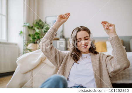 Young woman listening music trough headphones in her apartment. Young woman listening music trough headphones in her apartment. 101202850