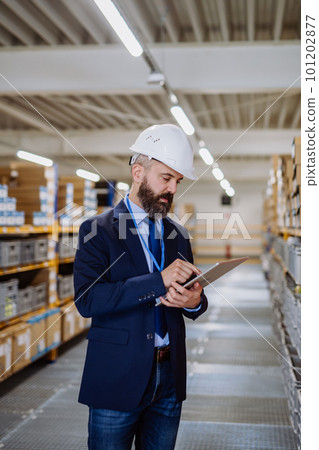 Manager in suit controlling goods in a waehouse. 101202877