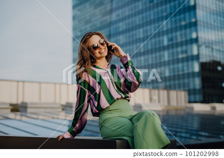 Portrait of beautiful young woman with smartphone outdoor in city, during sunset. 101202998