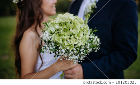 Close-up of bride and groom holding wedding bouquet, outdoor in the meadow. Close-up of bride and groom holding wedding bouquet, outdoor in the meadow. 101203023