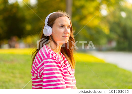 Relaxed woman sitting on the grass listening to music with headphones in a park 101203025