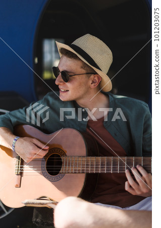 Young man sitting in van playing on the guitar and enjoying summer time. 101203075