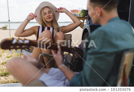 Young couple sitting together in front of van, camping and playing at guitair. 101203076