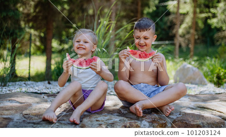 Little chidren sitting near lake and eating watermelon on hot sunny day during summer vacation. 101203124