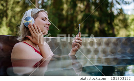 Reaxed woman with headphones listening to music in outdoor bathtub. Reaxed woman with headphones listening to music in outdoor bathtub. 101203132
