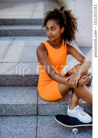 Multiracial teenage girl with backpack and skateboard, sitting and using smartphone in city during summer day. Multiracial teenage girl with backpack and skateboard, sitting and using smartphone in city during summer day. 101203181