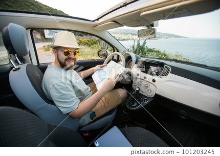 Hipster man looking on location navigation map in car, tourist traveler driving and hold in male hands europe cartography, view and plan tourist way road, trip in transportation cabriolet auto Hipster man looking on location navigation map in car, tourist traveler driving and hold in male hands europe cartography, view and plan tourist way road, trip in transportation cabriolet auto 101203245