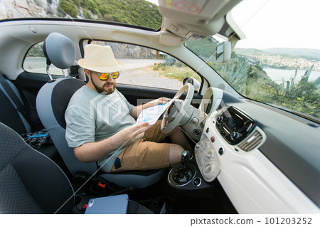 Hipster man looking on location navigation map in car, tourist traveler driving and hold in male hands europe cartography, view and plan tourist way road, trip in transportation cabriolet auto Hipster man looking on location navigation map in car, tourist traveler driving and hold in male hands europe cartography, view and plan tourist way road, trip in transportation cabriolet auto 101203252