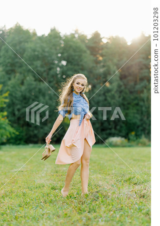 Smiling young woman in casual clothes strolls through the park. She is holding shoes in her hands. She is free and happy. The concept of freedom and youth 101203298