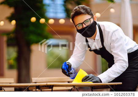Disinfecting to prevent COVID-19. Waiter in protective face mask and gloves cleaning. Disinfecting to prevent COVID-19. Waiter in protective face mask and gloves cleaning. 101203378