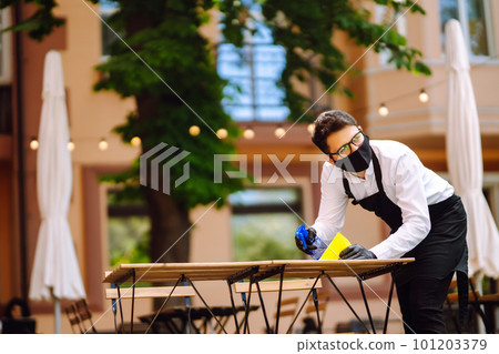 Disinfecting to prevent COVID-19. Waiter in protective face mask and gloves cleaning. Disinfecting to prevent COVID-19. Waiter in protective face mask and gloves cleaning. 101203379