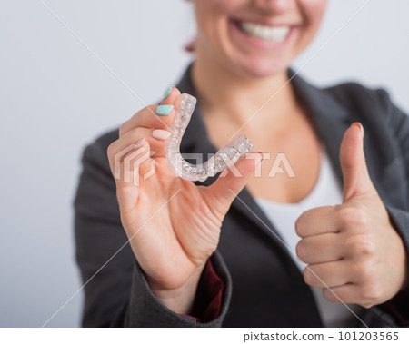 A woman in a jacket shows her thumbs up and demonstrates mouth guards to align the bite. The girl approves of the plastic removable braces for the teeth A woman in a jacket shows her thumbs up and demonstrates mouth guards to align the bite. The girl approves of the plastic removable braces for the teeth 101203565