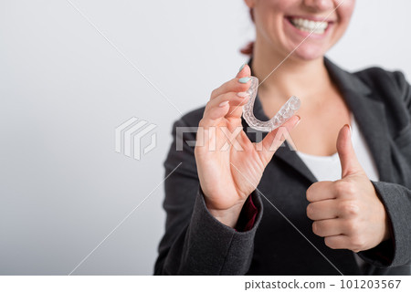 A woman in a jacket shows her thumbs up and demonstrates mouth guards to align the bite. The girl approves of the plastic removable braces for the teeth 101203567