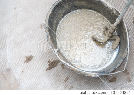 manual mixing of cement with the help of an electric mixer, cement in a bucket on a construction site manual mixing of cement with the help of an electric mixer, cement in a bucket on a construction site 101203895