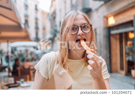 Happy woman eating traditional spanish delicious churros, a fried pastry with chocolate near a city cafe in Valence, Spain 101204071