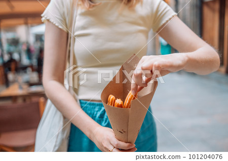 Happy woman eating traditional spanish delicious churros, a fried pastry with chocolate near a city cafe in Valence, Spain 101204076