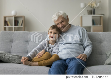 Happy grandfather hugging cheerful cute preschool boy on home sofa 101205346