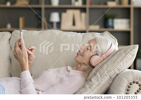Relaxed elder smartphone user woman in headphones listening to music Relaxed elder smartphone user woman in headphones listening to music 101205355