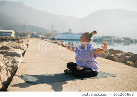 Mature old woman with dreadlocks practicing yoga and tai chi outdoors by the sea - wellbeing and wellness 101205668