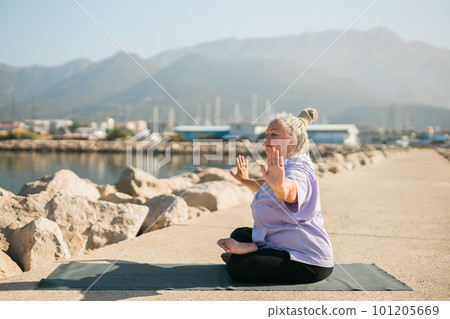 Mature old woman with dreadlocks practicing yoga and tai chi outdoors by the sea - wellbeing and wellness Mature old woman with dreadlocks practicing yoga and tai chi outdoors by the sea - wellbeing and wellness 101205669