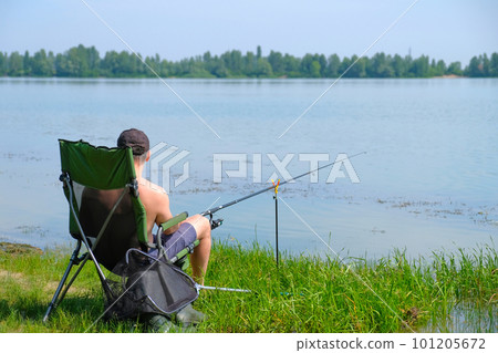 Fisherman on the river in a chair with a fishing rod in his hands. A man on summer fishing Fisherman on the river in a chair with a fishing rod in his hands. A man on summer fishing 101205672